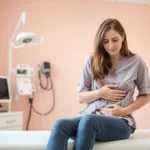 Recognizing UTI Symptoms: When to Seek Medical Help A worried woman holding her lower abdomen, sitting on a doctor's examination table, symbolizing UTI symptoms