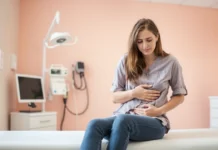 Recognizing UTI Symptoms: When to Seek Medical Help A worried woman holding her lower abdomen, sitting on a doctor's examination table, symbolizing UTI symptoms
