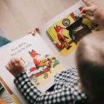 A joyful preschool teacher reading a colorful picture book to a diverse group of attentive toddlers in a cozy classroom reading nook featuring early literacy