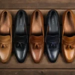 Loafers Style Guide: Best Types & How to Wear Them A stylish flat lay of various men's and women's loafers in leather and suede, placed on a wooden surface with soft shadows