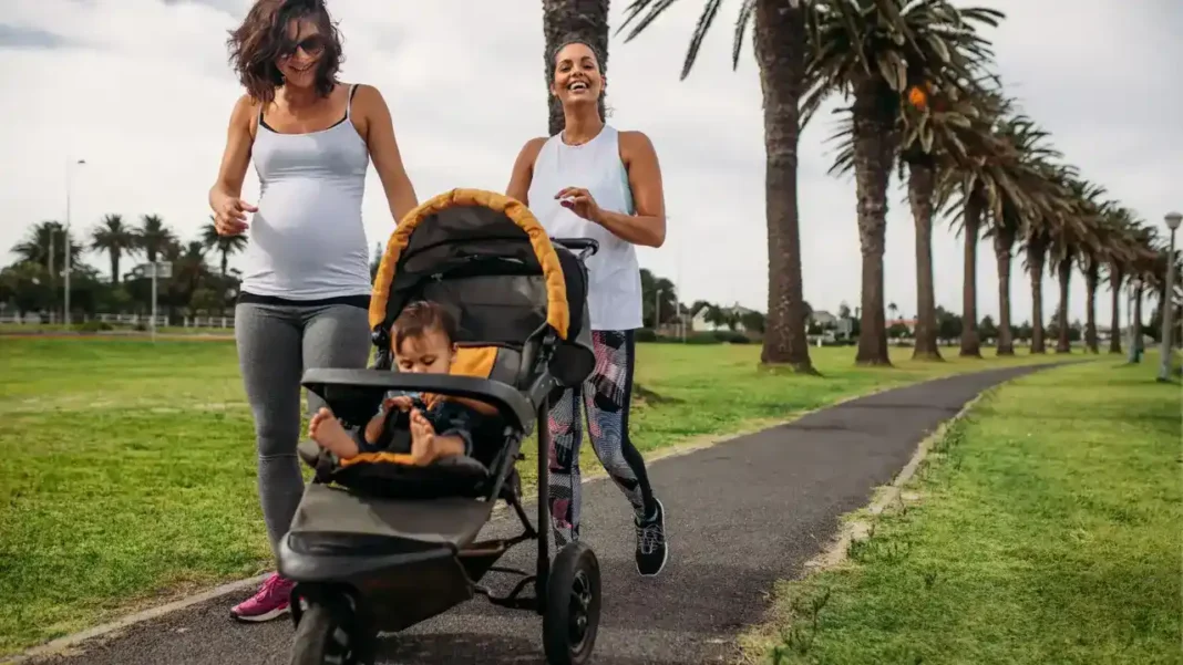 Professional lifestyle photo of an athletic mother in premium activewear jogging through an upscale urban park with a sleek, modern Jogging Stroller Pish Posh Baby