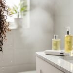 Low Porosity Hair Guide: Care, Products & Routine Close-up of curly hair with water beading on strands in a spa bathroom, representing low porosity hair care routine and hydration.