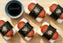 Homemade spam musubi wrapped in nori seaweed served on a wooden board with soy sauce dipping.