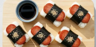Homemade spam musubi wrapped in nori seaweed served on a wooden board with soy sauce dipping.