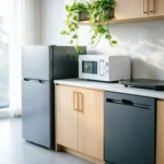 Modern small kitchen featuring compact appliances including mini fridge, microwave, and slim dishwasher in a bright, minimalist space.